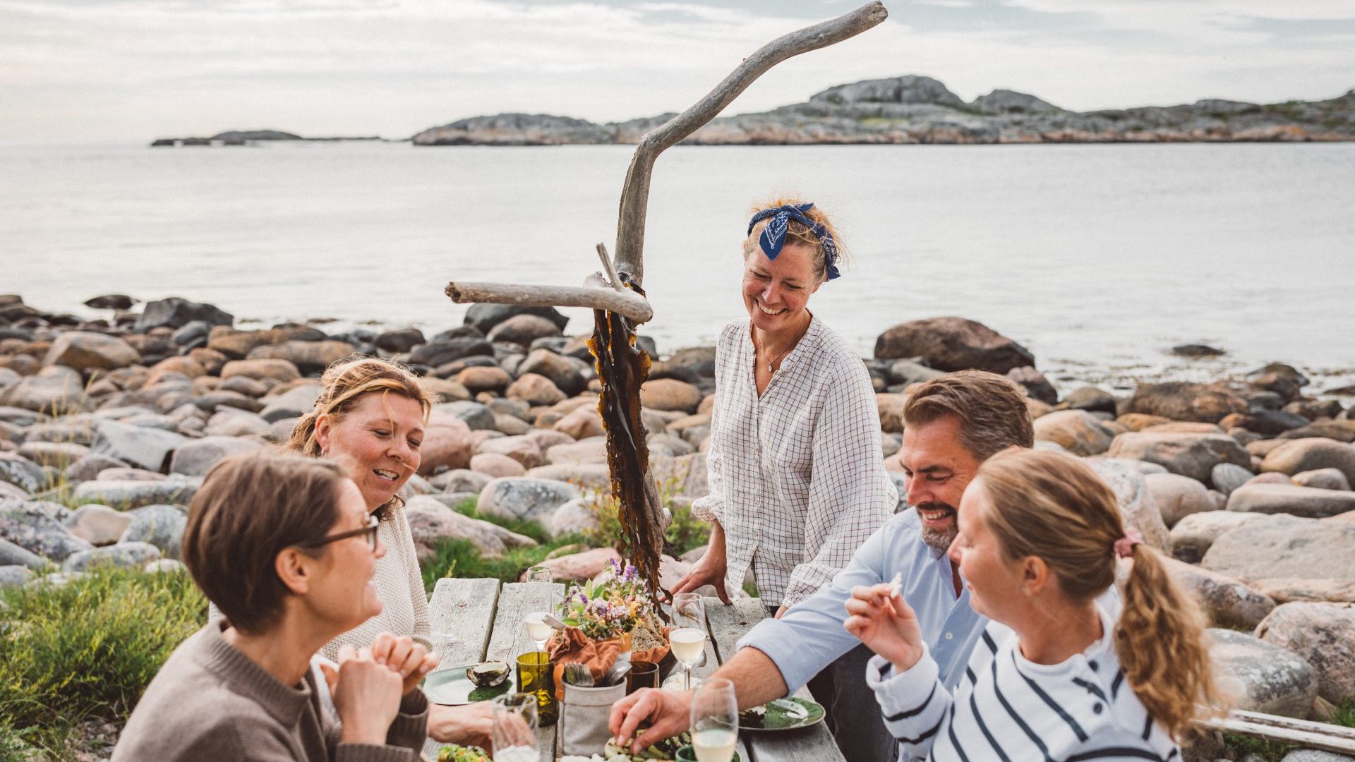 A group gather for a meal on a rock shoreline.