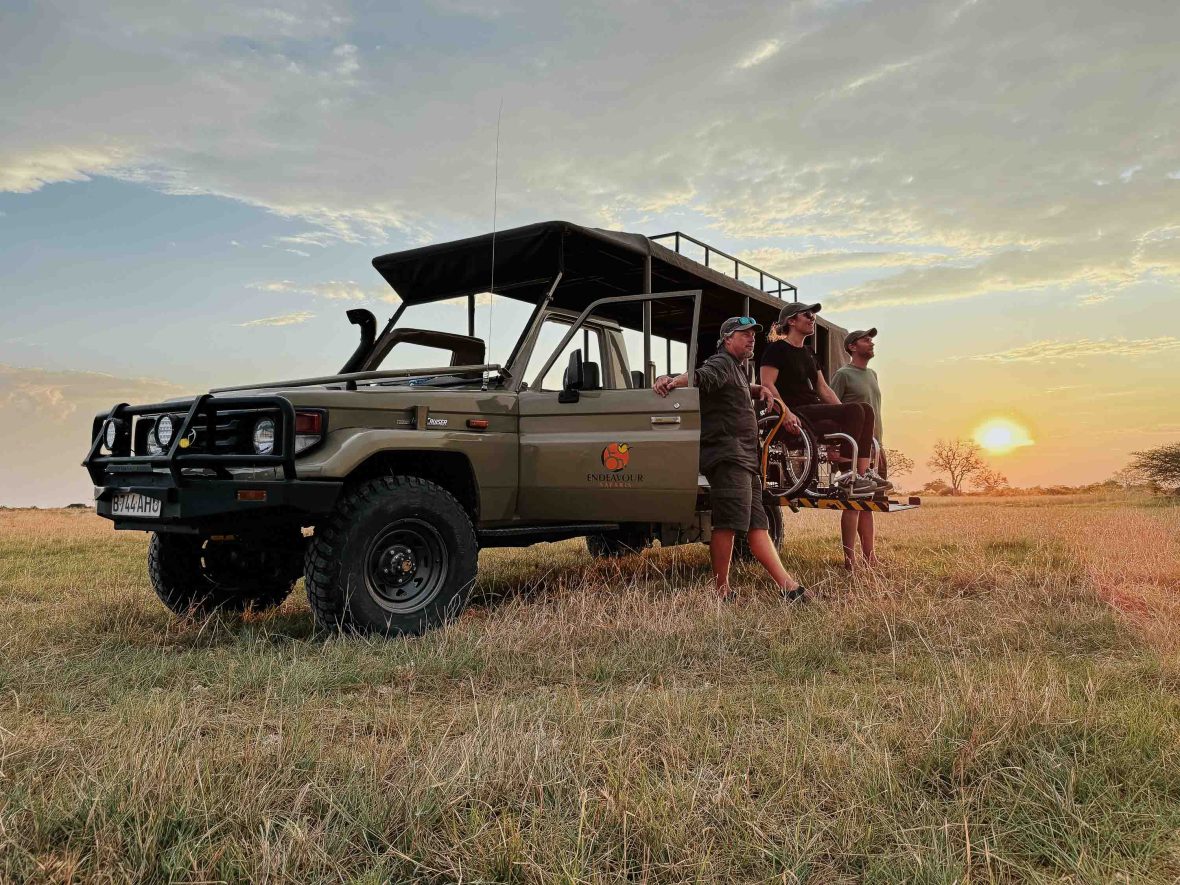 Three people watch sunset from a safari vehicle.