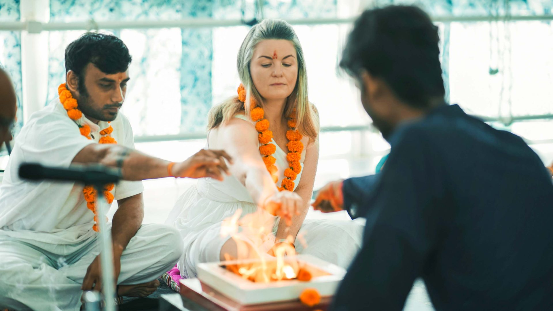 A woman with blonde hair lights candles with some Indian men in a ceremony.
