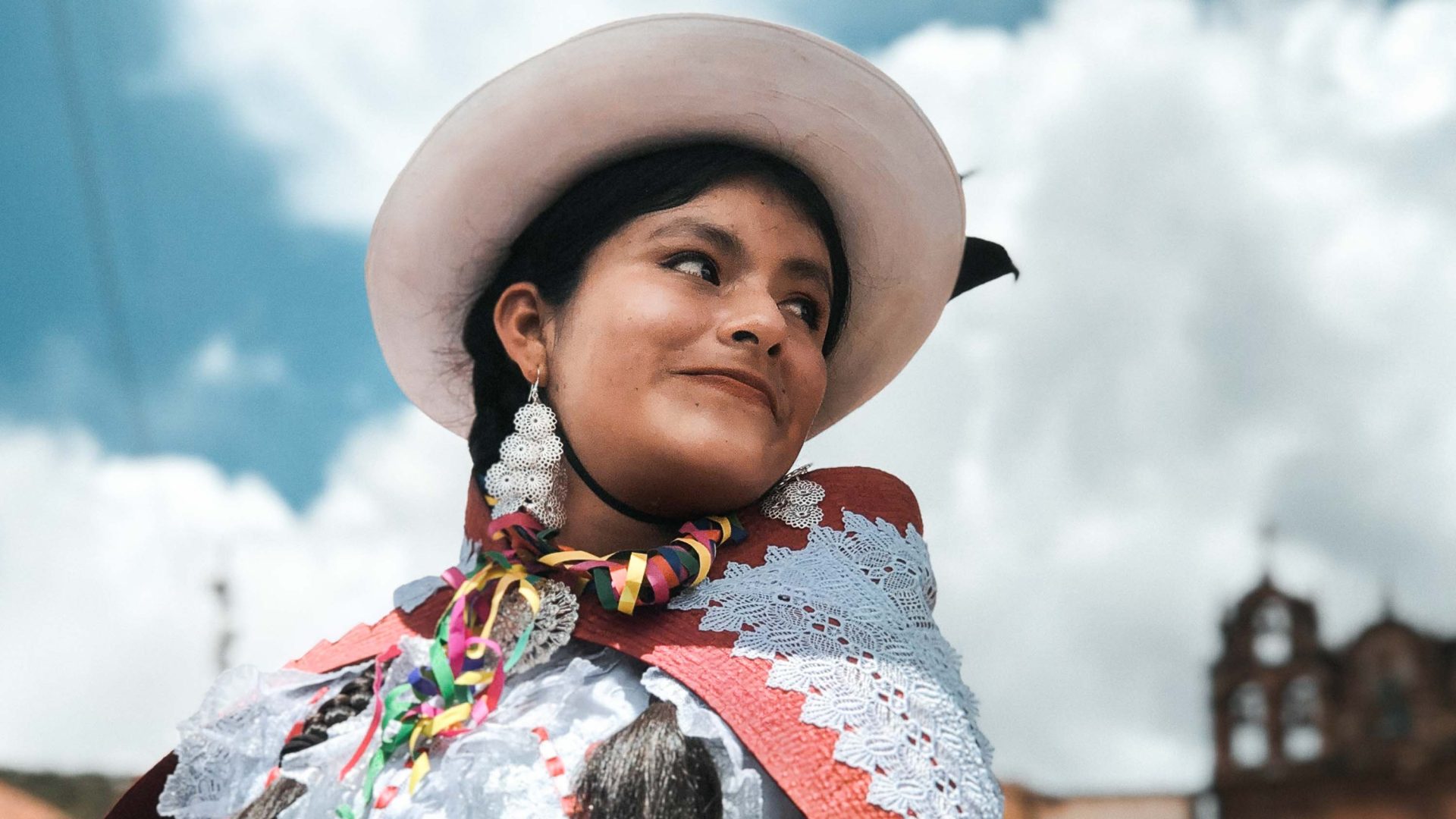 A woman in a hat and traditional Bolivian clothing smiles and looks away from the camera.