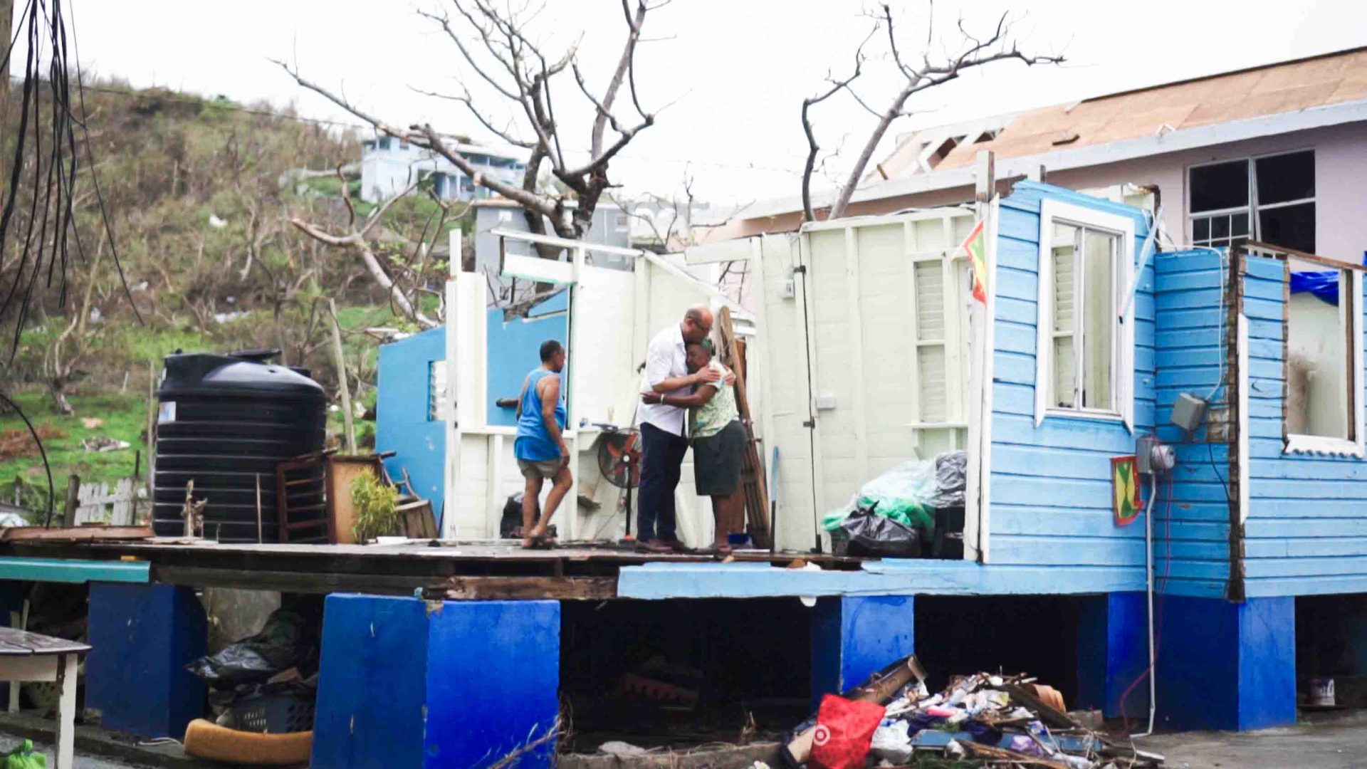 Two people hug each other while standing in what little remains of their home.
