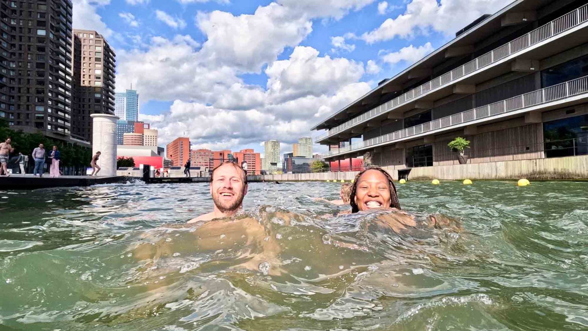 A woman and a man smile for the camera while swimming in a river.