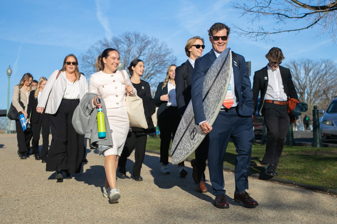 Team wearing suits and carrying surfboards walk down path
