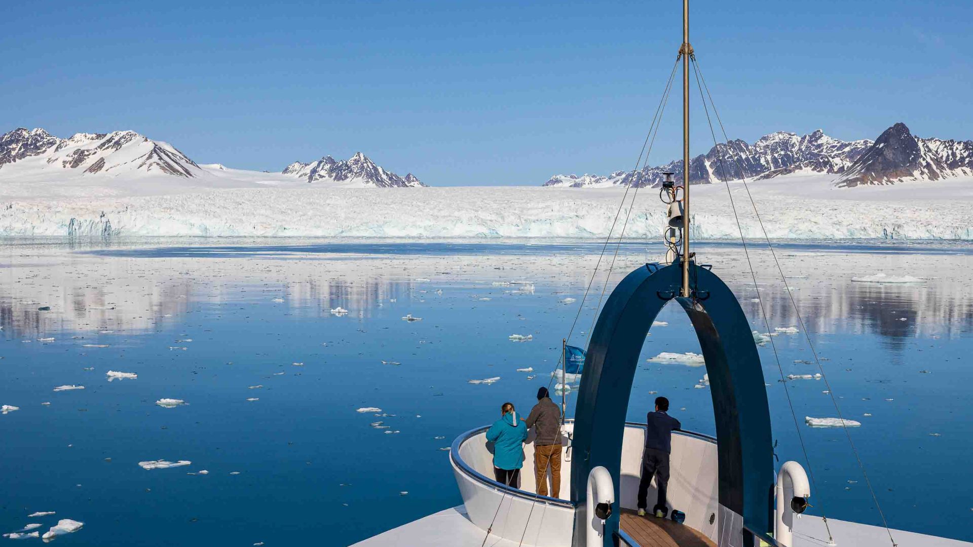People look out from the front of a ship toward icebergs.