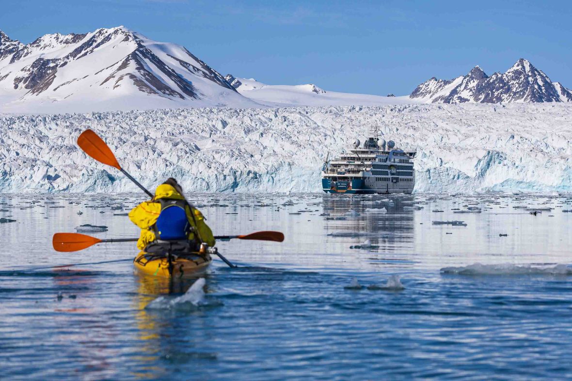 A person kayaks in the direction of the cruise ship and also a glacier.