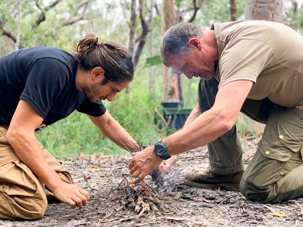 A man shows another man how to build a fire.