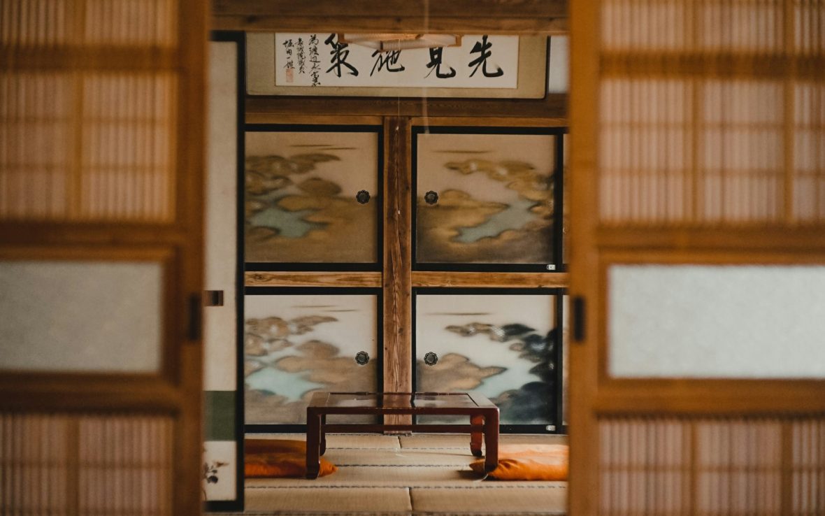 Inside a tatami-mat floored room, with a small table and cushions. Japanese art hangs on the walls.