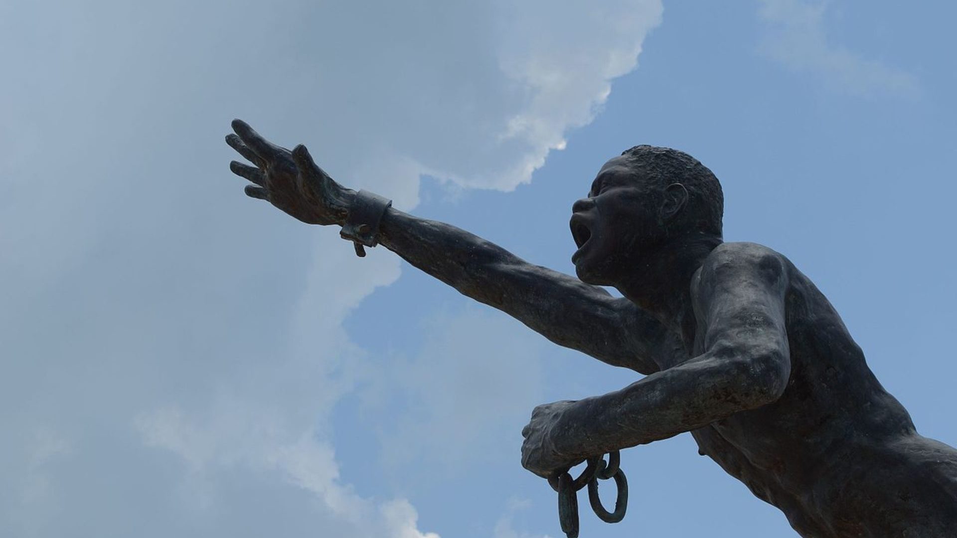 Statue of man in chains reaching to sky.