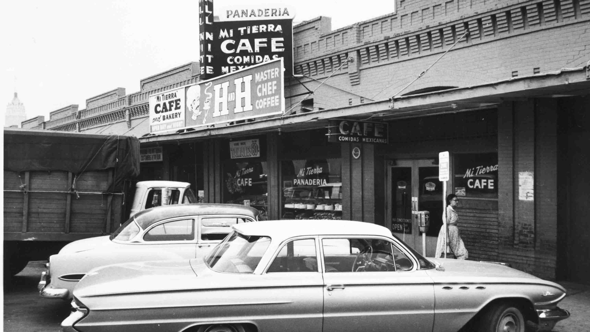A black and white photo of a restaurant with cars parked out front.