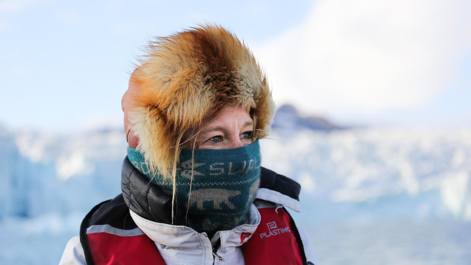 A woman in a hurry hat and a mouth covering looks away.