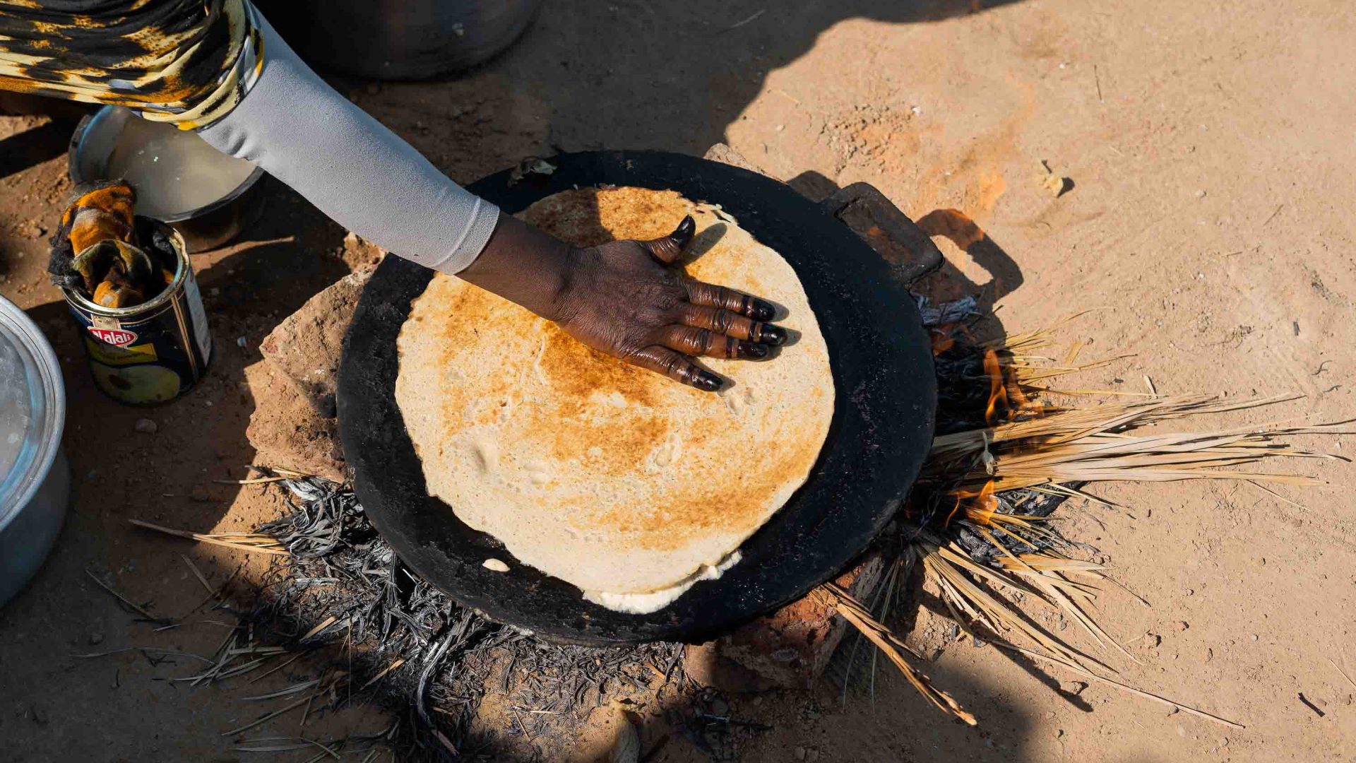 A hand flips a pancake on an oven on the ground.